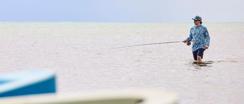 An angler wades through the ocean with fly rod in hand
