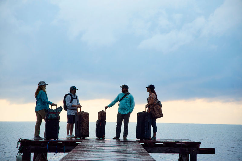 A group of people with their luggage standing at the end of a dock during sunrise.