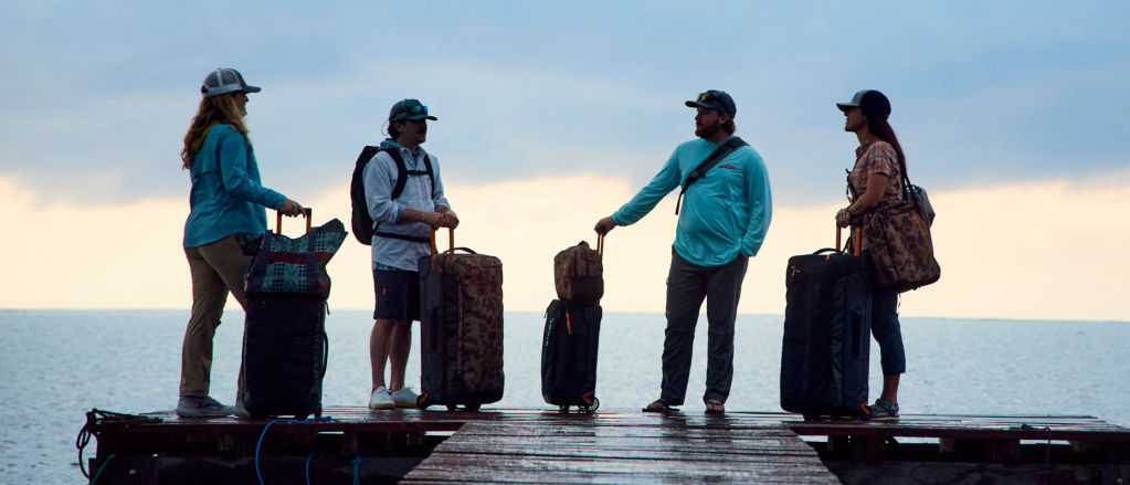 A group of people with their luggage standing at the end of a dock during sunrise