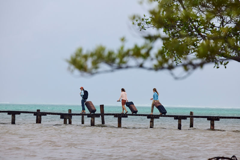 Three people rolling luggage down a dock by the ocean