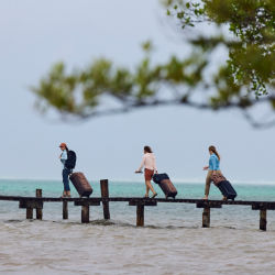 Three people rolling luggage down a dock by the ocean