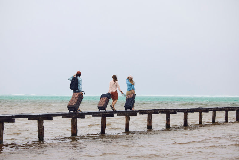 A group of people with their luggage standing at the end of a dock during sunrise.