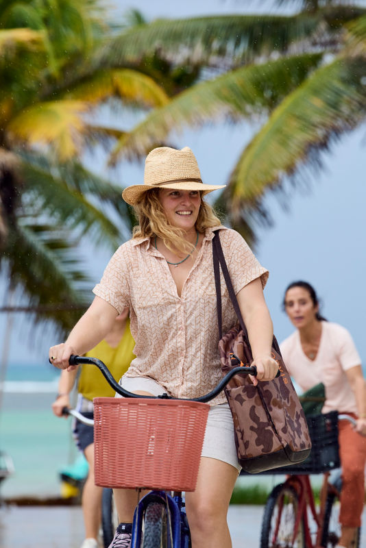 A woman with a camo bag on her shoulder riding a bike with a basket