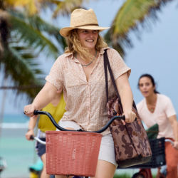 A woman with a camo bag on her shoulder riding a bike with a basket