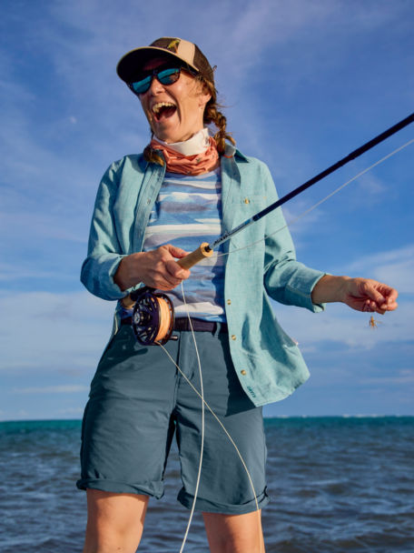 Woman in Alpine Lake Tech Chambray Shirt handles her rod on a skiff.