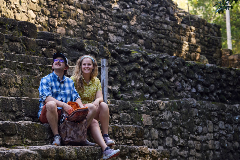 A man and a woman sitting on stone steps with a camo bag.