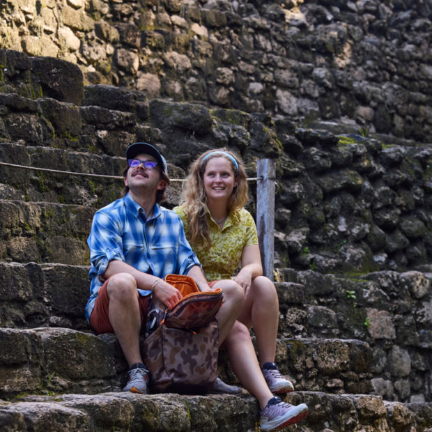 A man and a woman sitting on stone steps with a camo bag