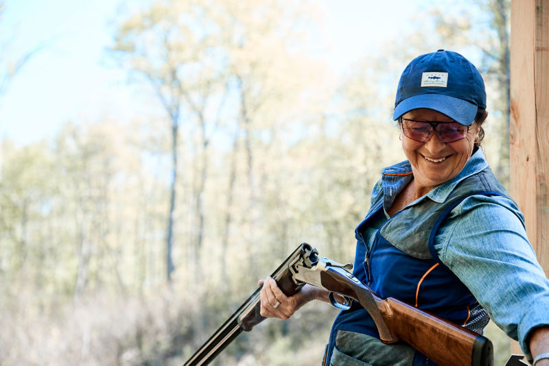A smiling woman reloads a shotgun for clays shooting.
