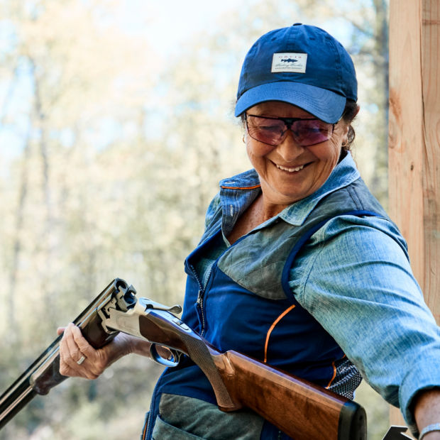 A smiling woman reloads a shotgun for clays shooting.