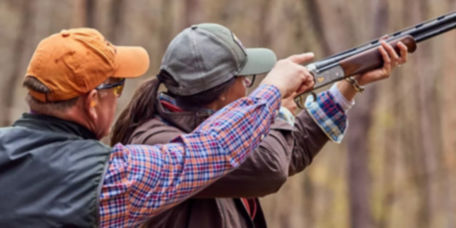 An instructor teaches a woman how to aim a shotgun