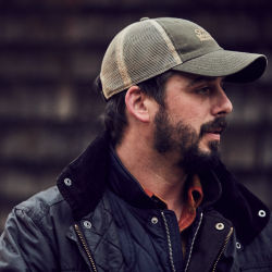 A man wearing a trucker cap and Barbour jacket looks to the right.