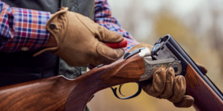 A gloved hand loads a broken-open shotgun.