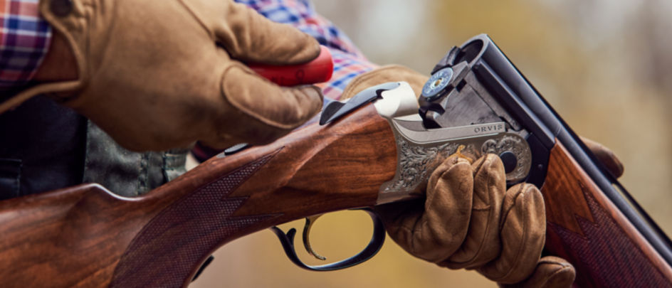 A close-up of a gloved hand, loading shells into a shotgun.