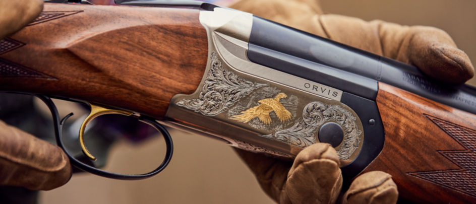 The intricate details of an Orvis ELOS over-under shotgun held in two leather-gloved hands.
