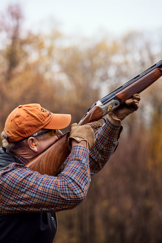 A wingshooter in an orange cap aims his shotgun