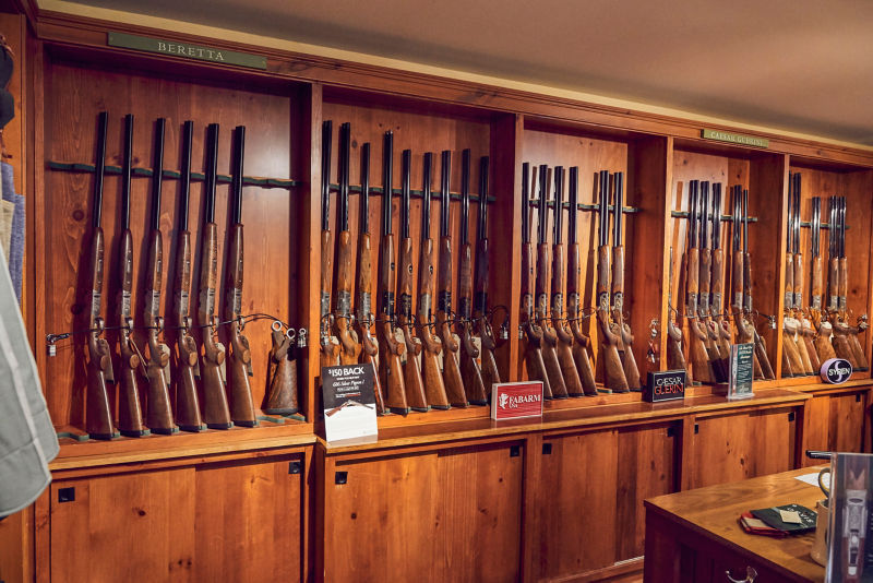 Wooden racks of shotguns line the wall of Orvis's Sandanona Shooting Grounds.