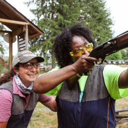 A female instructor stands behind another woman shooting.