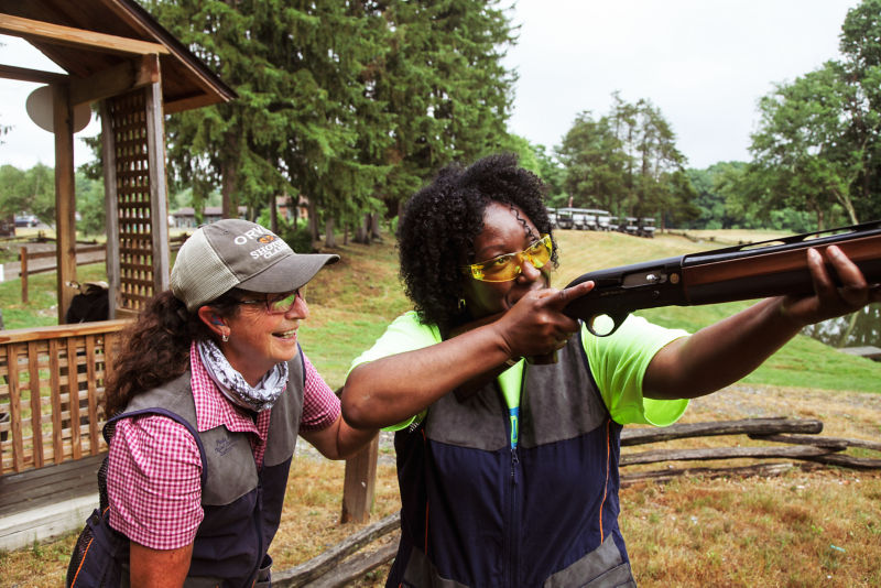A shooting instructor teaching a student how to aim her shotgun.