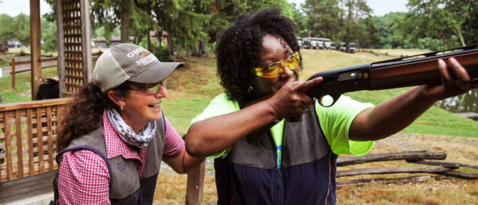 A shooting instructor teaching a student how to aim her shotgun.