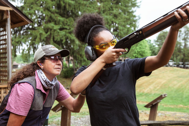 A shooting instructor guides a woman in proper technique