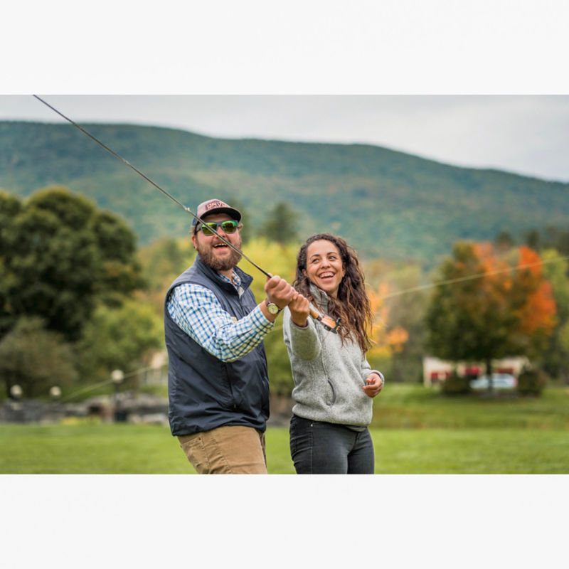 Woman laughing with fly fishing instructor while they both hold a rod.
