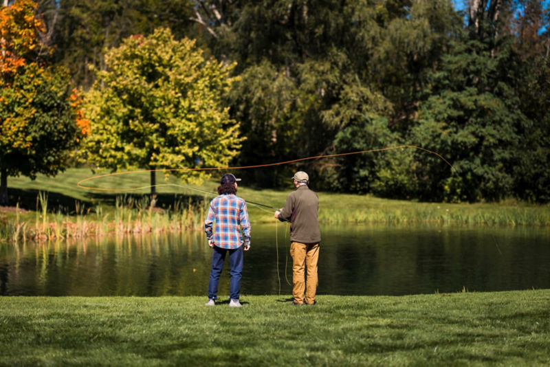 An instructor shows a student how to cast into a pond.