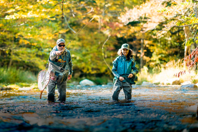 Two people fly fish from knee-deep in a stream.