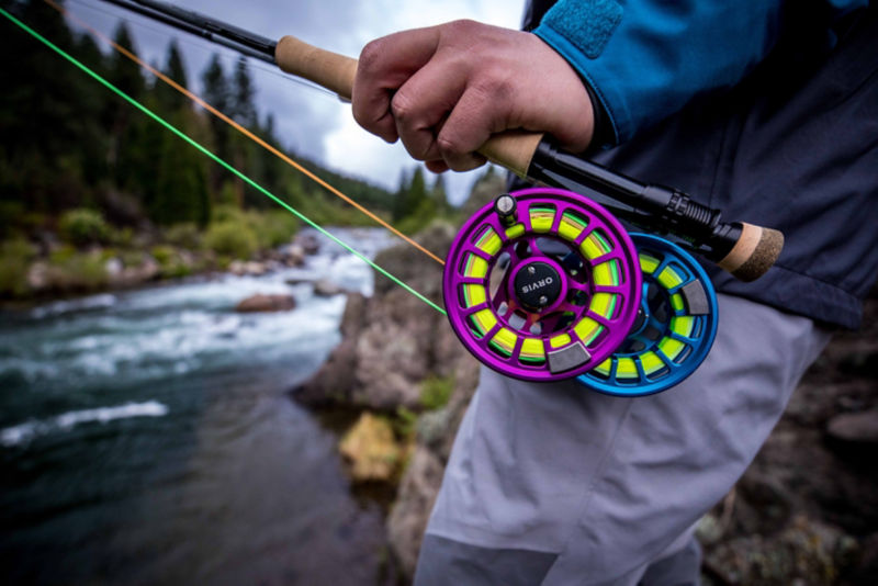 A hand holding two fly rods with bright colored fly reels and line.