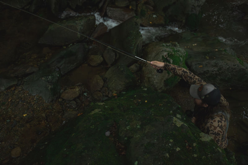 An angler with a camo jacket wading in a rocky river.