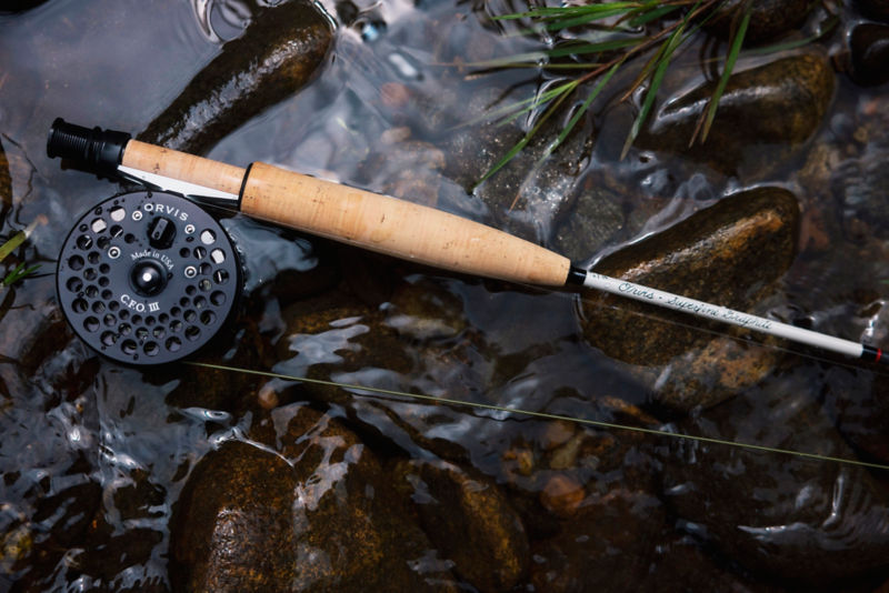 A fly rod lays on a rock half in the stream.
