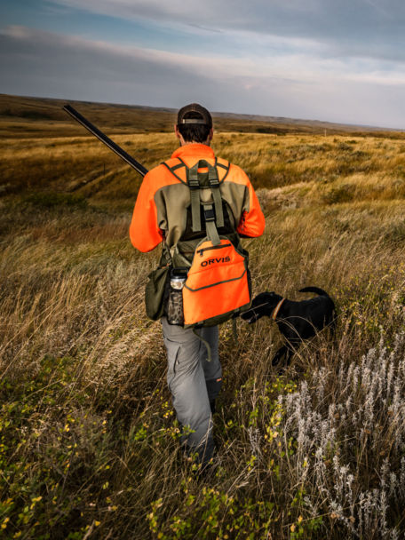 Hunter wearing a PRO Series Hunting Vest and his dog walk through tall grass.