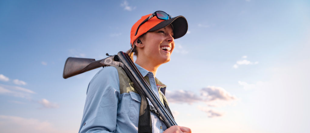 A hunter carrying a shotgun on her shoulder.