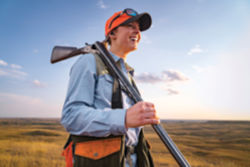 A hunter holding an unloaded shotgun in a field