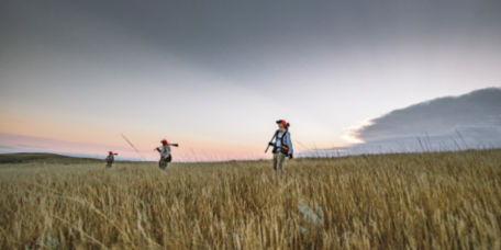 Three hunters walking through a field of tall grass at dusk