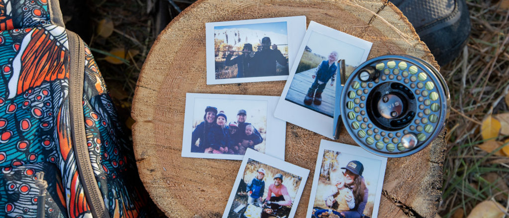 A group of 5 Polaroid photos laid on a stump next to a fly reel.