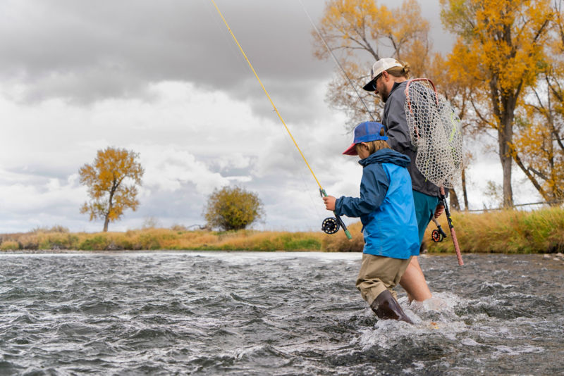 A parent and child, fly rods in hand, pick their way down to a stream