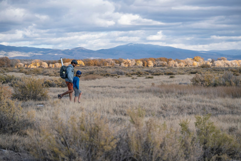 Two hikers walk through the wide Wyoming plain with mountains in the background.