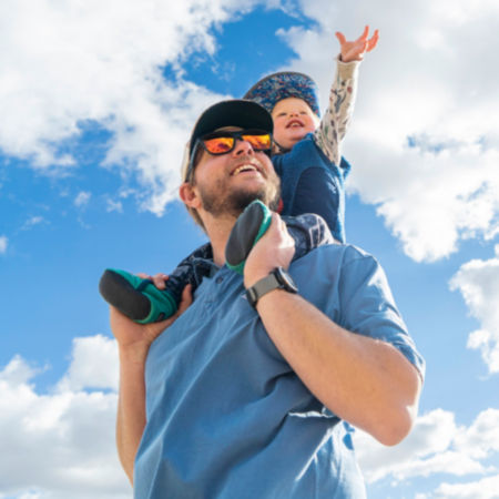 A son riding on top of his father's shoulders while reaching for the sky.