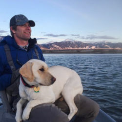 Steve Hemkens with his golden Labrador on his lap in a boat on a lake