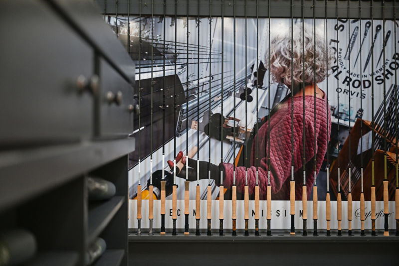 A fly rod repair expert working at the Orvis Rod Shop seen through a line of fly rods standing on end.