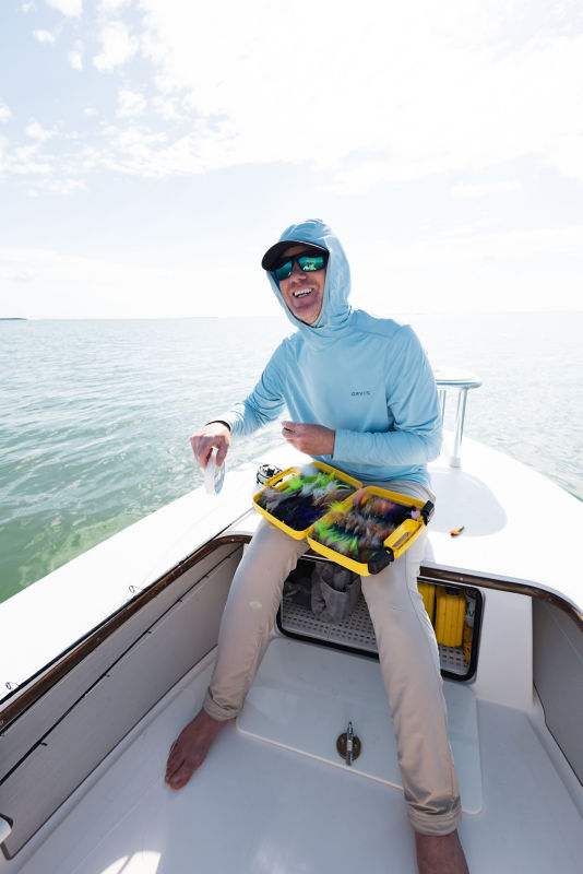 A close-up of an angler wearing a loaded fishing vest holds a trout above their net.