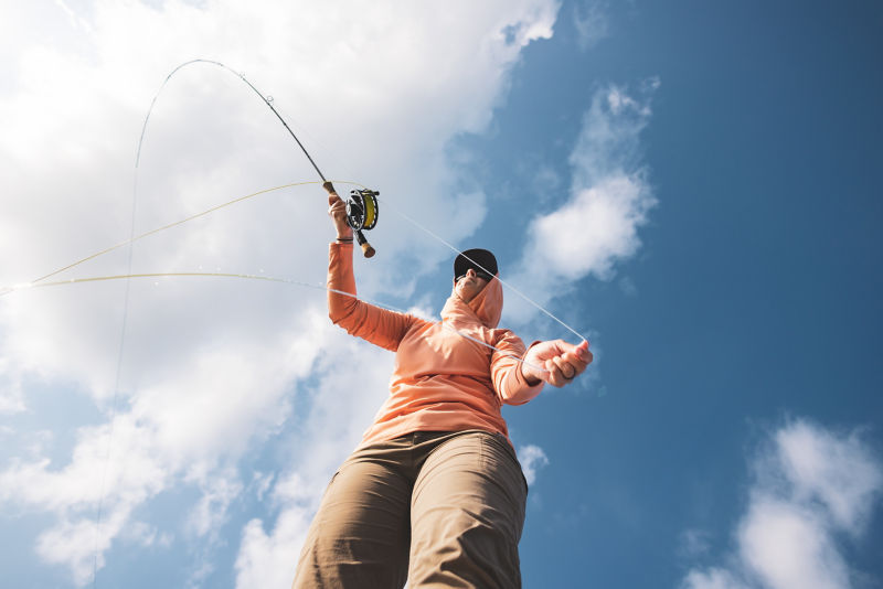 A saltwater angler mends her line from the front of a boat.