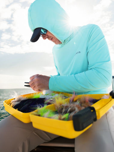 An angler picks a fly out of a giant yellow fly box.