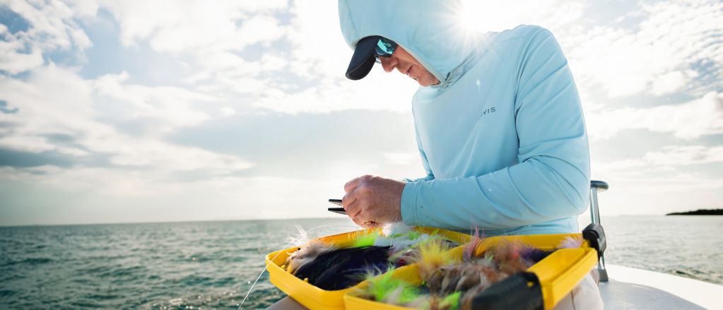 An angler in a small boat on the ocean picks through a flybox.