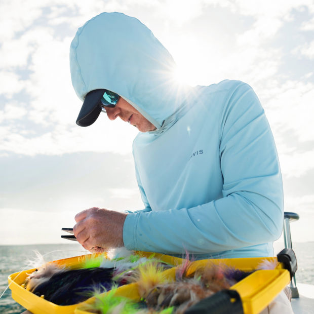 A close up on a man wearing a UPF protective shirt and picking through his fly box.