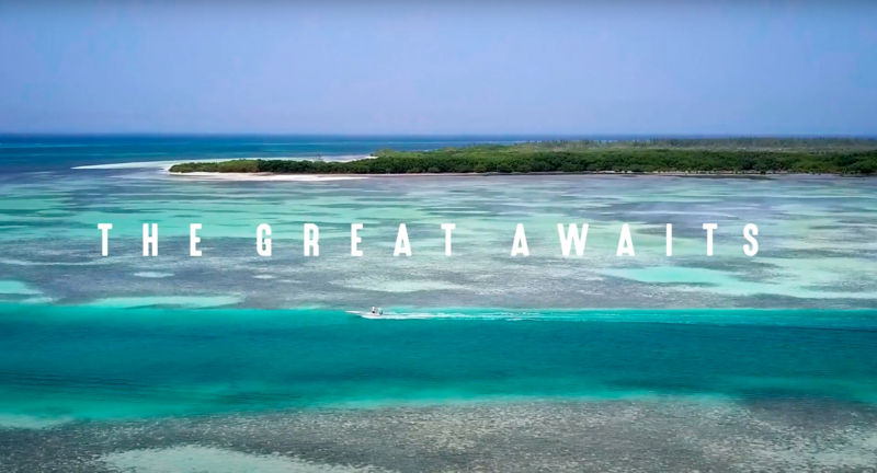 A drone-view of turquoise ocean with a small boat and a green island.
