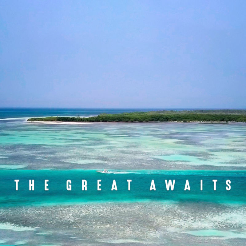 A drone-view of turquoise ocean with a small boat and a green island.