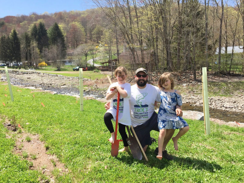 A father and his two daughters standing next to a stream.