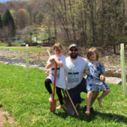 A father and his two daughters standing next to a stream.