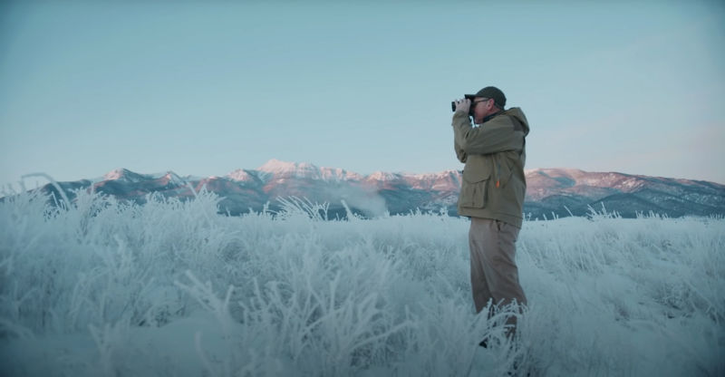 man in frozen field looking through binoculars